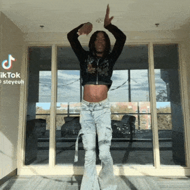 a man in a crop top and jeans is dancing in front of a window with tiktok steveuh written on the bottom