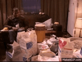a man is sitting on a couch in a messy room surrounded by boxes of milk