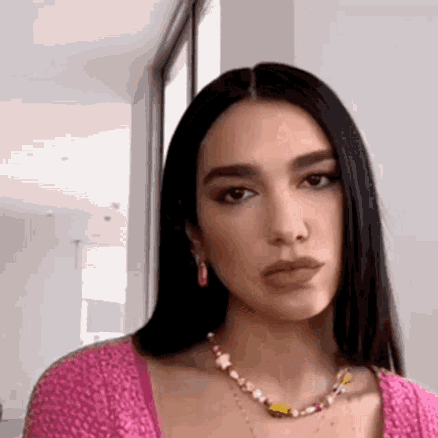 a woman wearing a pink top and a necklace is making a funny face .