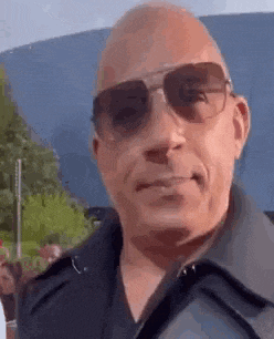 a bald man wearing sunglasses and a black shirt is smiling .