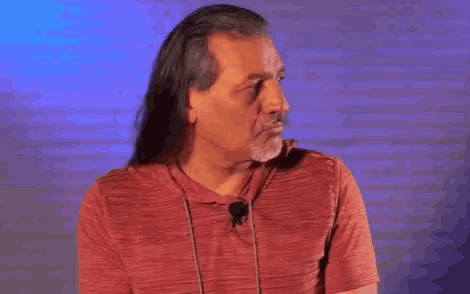 a man with long hair and a beard is pointing at something in front of a blue background .