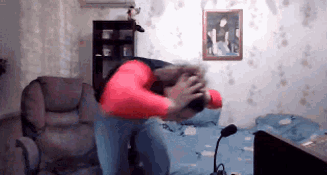 a man in a red shirt is standing in a living room with his head in his hands