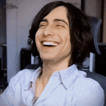 a young man with long hair is laughing with his eyes closed and wearing a striped shirt .