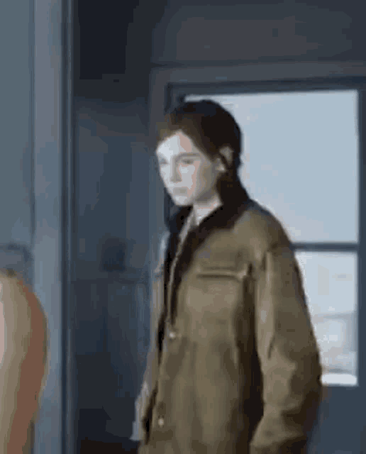 a woman in a jacket is standing in front of a window in a room .