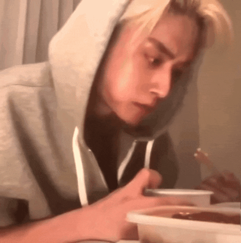a man wearing a hoodie is eating food from a container
