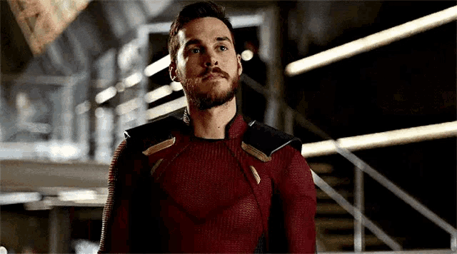 a man with a beard is wearing a red superhero costume and standing next to stairs .