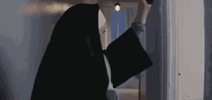 a nun in a black robe is standing in a doorway holding a book .