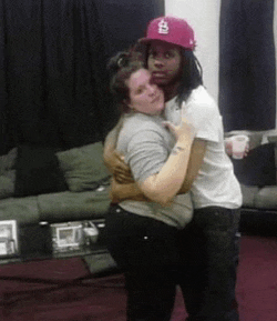 a man and a woman are hugging each other in a living room . the woman is wearing a pink hat .