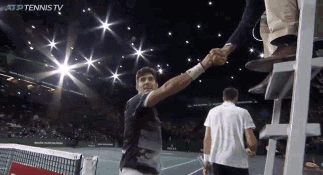 a tennis player shakes hands with a referee while atp tennis tv is shown in the background