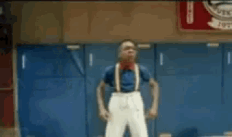 a young man wearing suspenders and a blue shirt is standing in a gym .