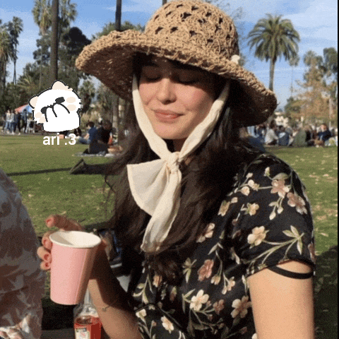 a woman wearing a straw hat and a floral shirt is holding a cup