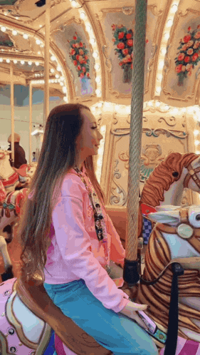 a girl is riding a merry go round in a pink sweatshirt
