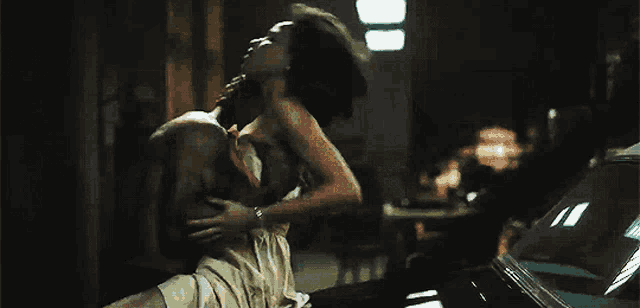 a man and woman are kissing in a dark room in front of a car