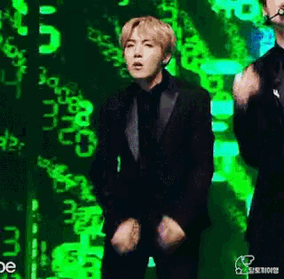 a man in a black suit is dancing on a stage in front of a green background .