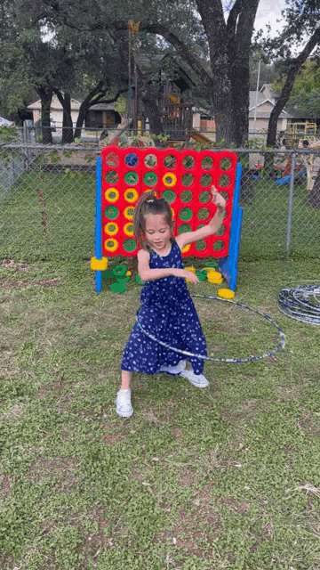 a little girl is playing with a hula hoop in front of a giant connect four board