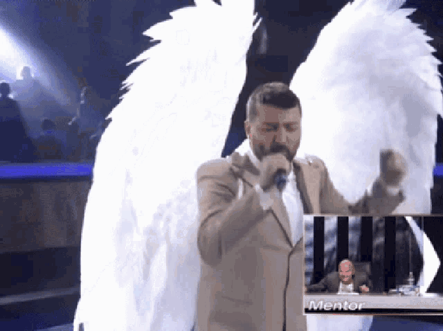 a man with angel wings sings into a microphone