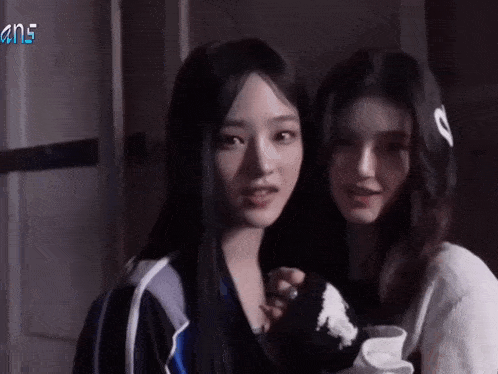 two young women are standing next to each other in a dark room and looking at the camera .