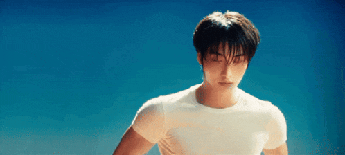 a young man wearing a white t-shirt is standing in front of a blue sky .