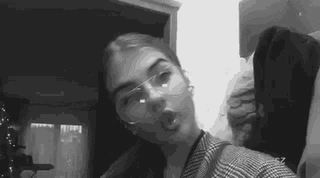 a black and white photo of a girl wearing glasses and a plaid jacket .
