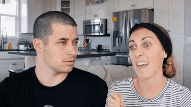 a man and a woman are looking at each other in a kitchen with a refrigerator in the background