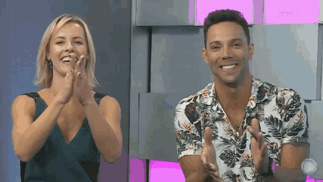 a man and a woman are clapping in front of a wall