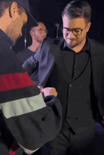 a man in a suit and glasses is being helped by another man in a hat