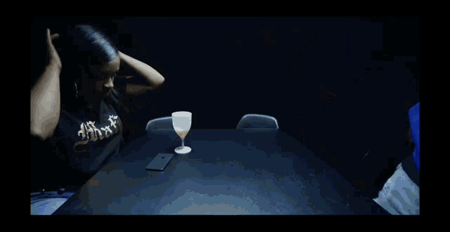 a woman sitting at a table with a glass of wine and a cell phone