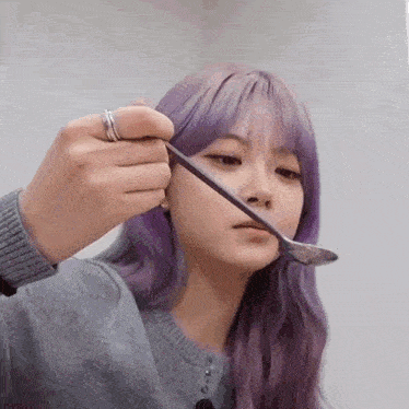 a girl with purple hair is holding a spoon to her face .