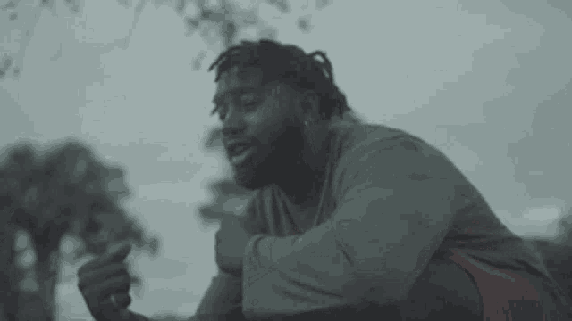 a man with dreadlocks and a beard is sitting on the ground and pointing at something .