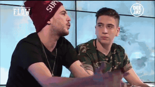 two young men are sitting next to each other and one has a supreme hat on