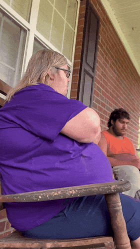 a woman in a purple shirt sits on a porch with a man in an orange shirt