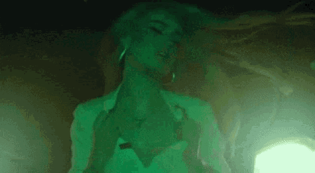 a woman in a white shirt is dancing in a dark room with green lights .
