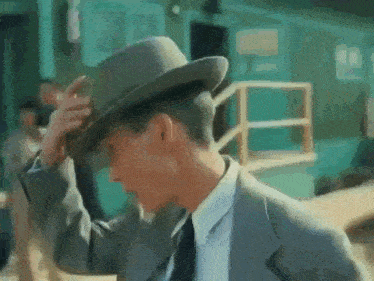 a man in a suit and tie is putting on a hat
