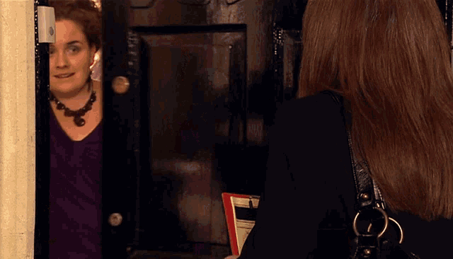 a woman in a purple shirt talks to another woman in a black jacket