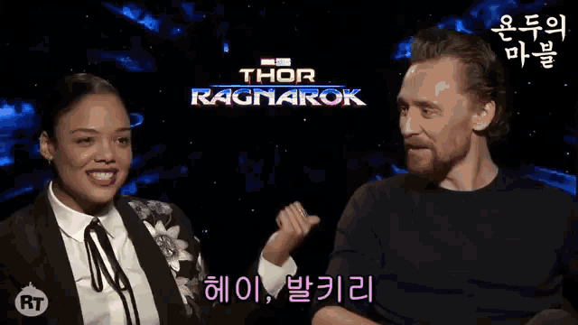 a man and a woman are sitting next to each other in front of a thor ragnarok poster .
