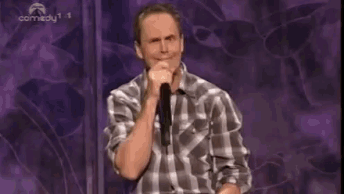 a man in a plaid shirt is holding a microphone in front of a comedy 1 logo
