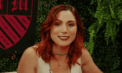 a woman with red hair is smiling in front of a shield that says uc