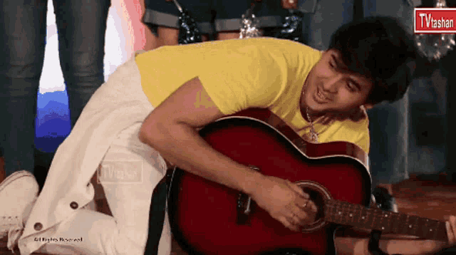 a man in a yellow shirt is playing a red guitar in front of a tv vasan sign