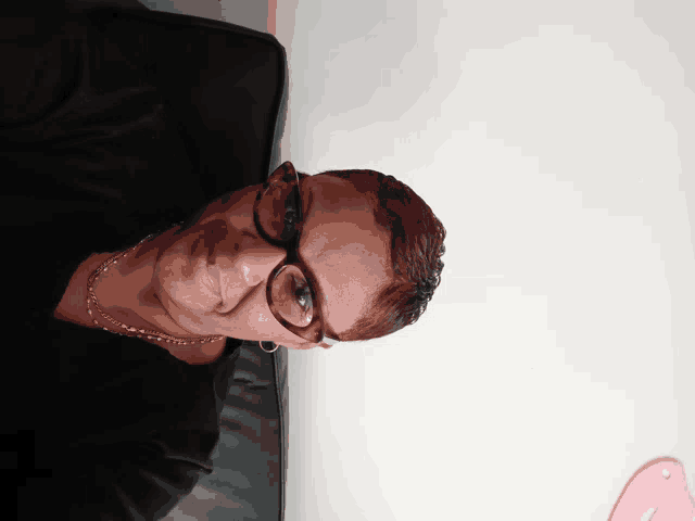 a woman wearing glasses and a necklace sits on a couch