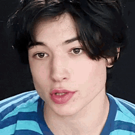 a young man wearing a blue and white striped shirt looks at the camera .