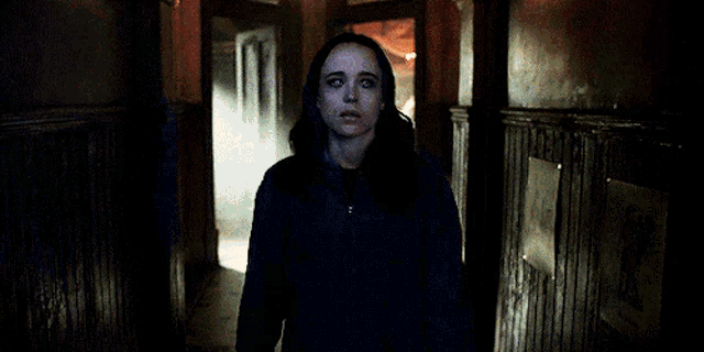 a woman in a blue jacket is standing in a dark hallway looking at the camera .