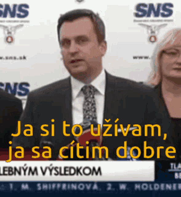 a man in a suit and tie is standing in front of a sns sign