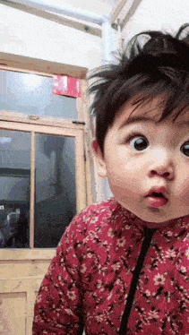 a baby in a red floral outfit looks surprised