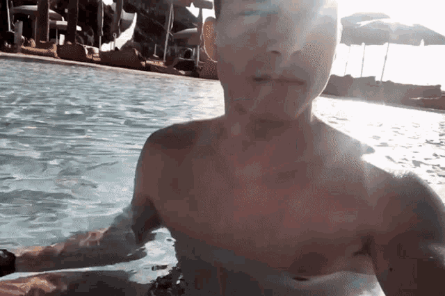 a shirtless man in a swimming pool with umbrellas in the background