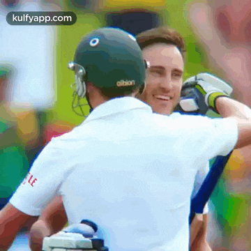 two cricket players are hugging each other and one of them is wearing a helmet that says ' oltsion ' on it