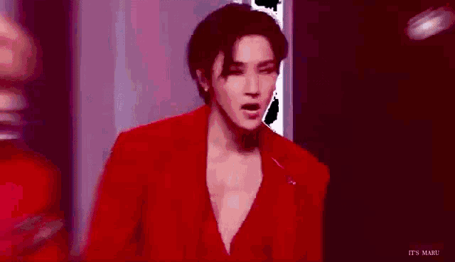 a man in a red suit is standing in front of a window in a room .