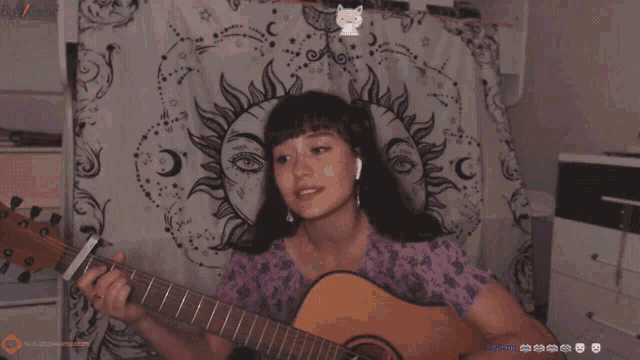 a woman is playing a guitar in front of a tapestry with the sun and moon on it