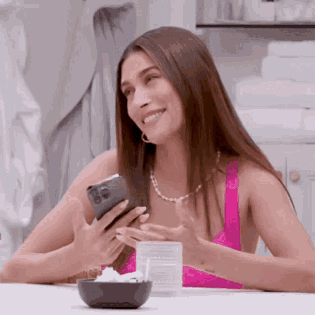 a woman in a pink top is smiling while looking at her phone