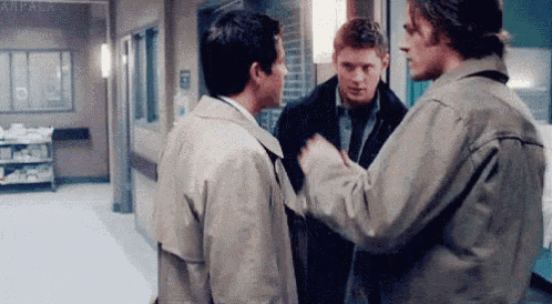 three men are standing next to each other in a hallway in a hospital talking to each other .