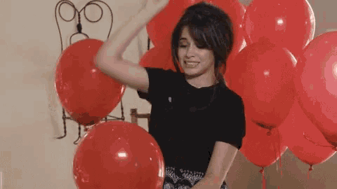 a woman in a black shirt is dancing in front of a bunch of red balloons